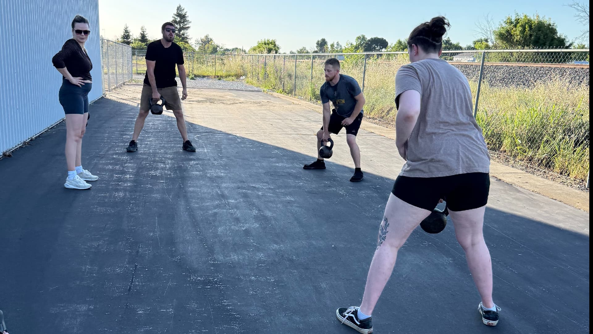 Group fitness training on a blacktop area behind a business building in Chico, CA — coworkers doing kettlebell squats together during a mobile corporate wellness session with Gym Truck Chico